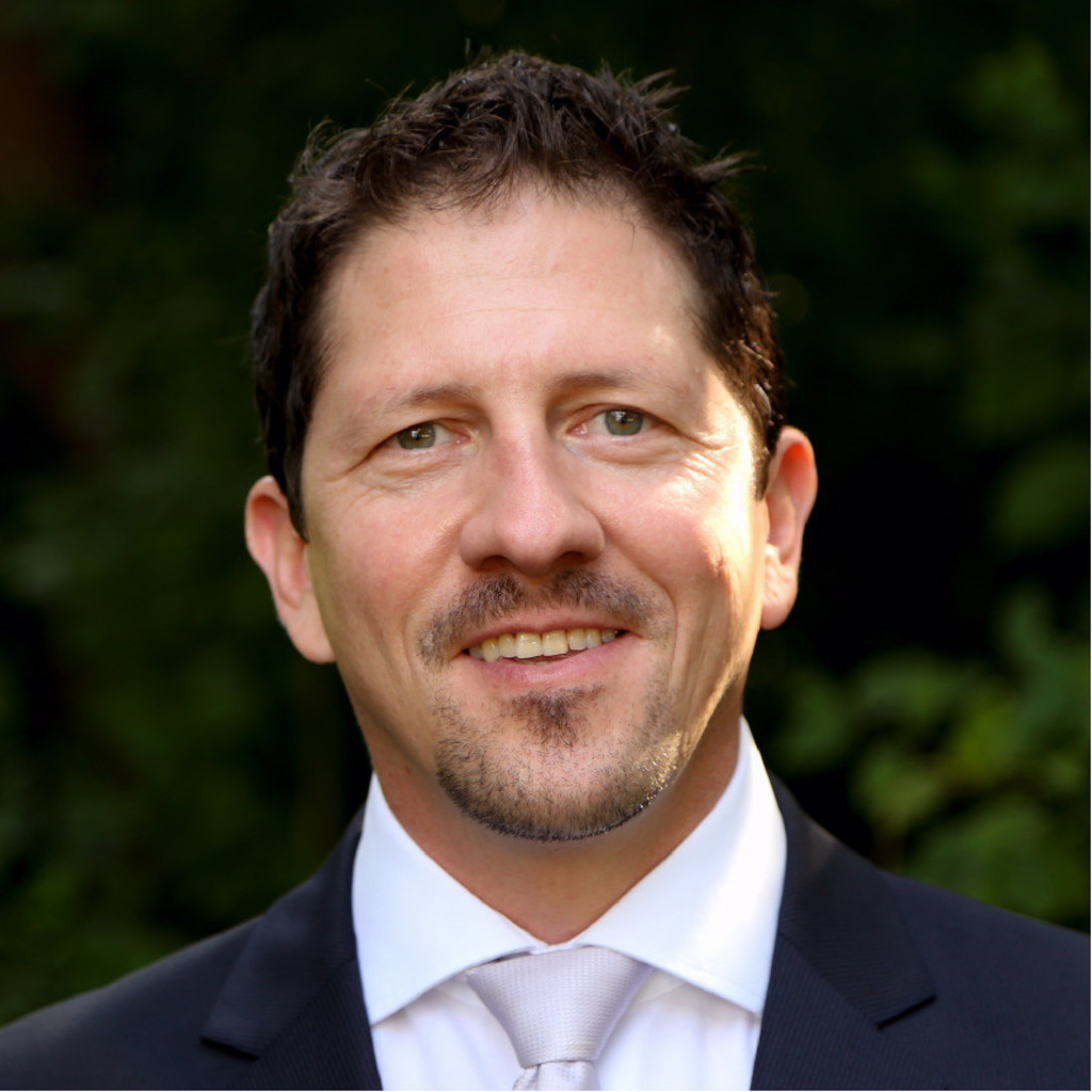 Roland Sing, ein Herr mitttleren Alters mit dunklen kurzen Haaren, 3 Tage Bart und Anzug.